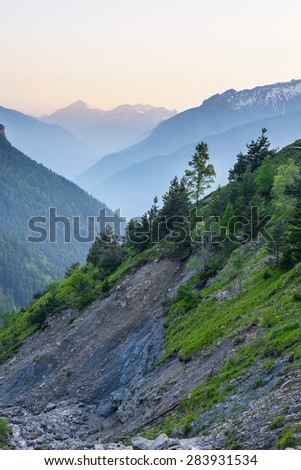 Mountain stream flowing in very steep valley with landslides and erosions on rocky slopes. Shot at dusk in the italian Alps with foggy valleys below and soft light.