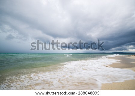 Dramatic cloudscape with heavy rain and tropical storm at the horizon on the coastline of Tanjung Karang, Central Sulawesi, Indonesia. Wide angle shot with waves in the foreground, blurred motion.
