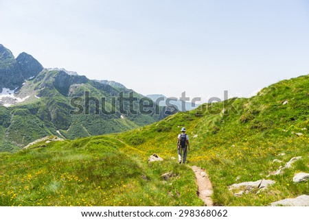 One backpacker hiking uphill on footpath in the italian Alps. Summer adventures and exploration on the Alps. Wide panoramic view from above.