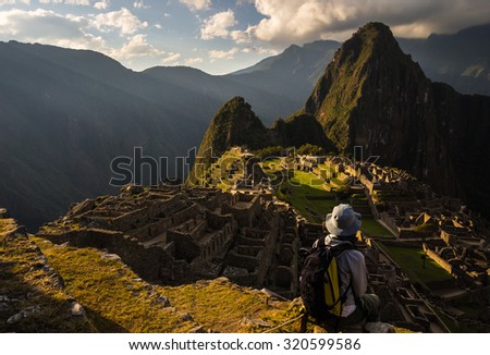 Machu Picchu illuminated by the last sunlight. The Inca\'s city is the most visited travel destination in Peru. One person sitting in contemplation.