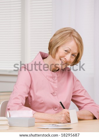 Smiling senior woman paying bills with checks at desk