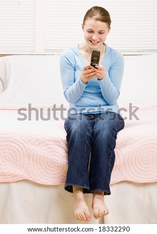 Casual teenage girl sitting on bed text messaging on cell phone