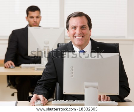 Happy businessman working on computer with co-worker in background