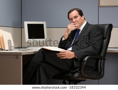 Serious businessman thinking at desk in cubicle