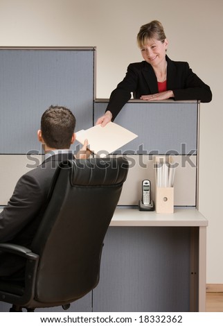 Businesswoman handing co-worker file folder at desk in cubicle