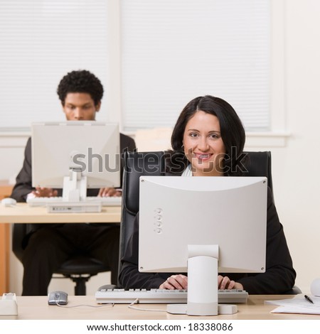 Happy businesswoman working on computer with co-worker in background