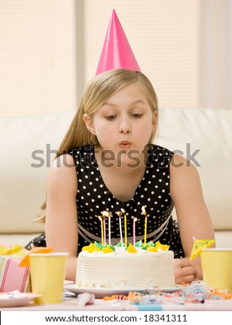 Excited girl in party hat blowing out candles on birthday cake at party