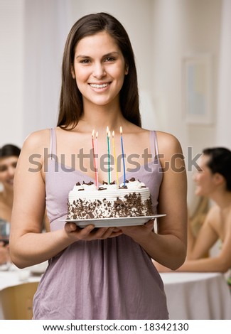 Generous woman holding lighted birthday cake about to surprise friends