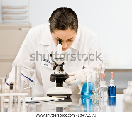 Curious research scientist in lab coat and rubber gloves looking at specimen under microscope in laboratory