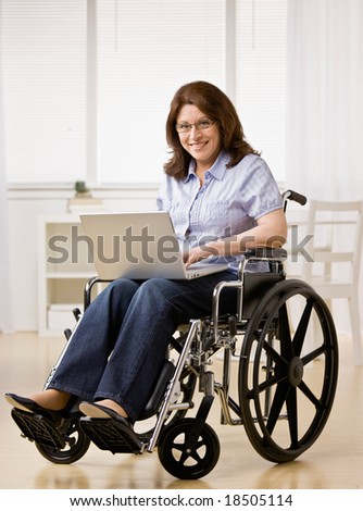 Disabled woman sitting in wheel chair typing on laptop