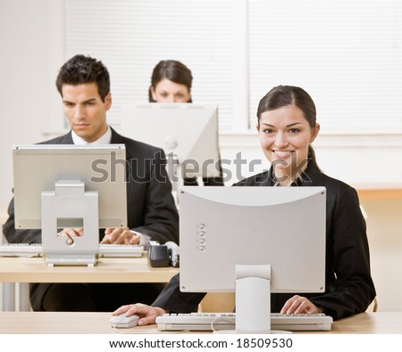 Businesswoman working on computer with co-workers in background