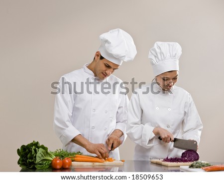 Chefs in toques and chef?s whites preparing and chopping fresh vegetables together