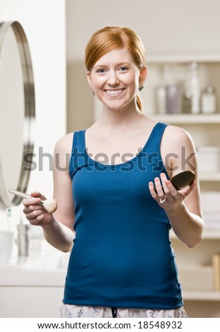 Woman in pajamas in bathroom applying blush with makeup brush