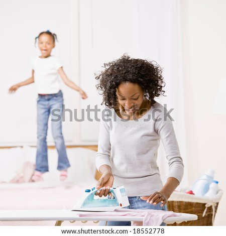Housewife ironing laundry while mischievous girl jumps on bed