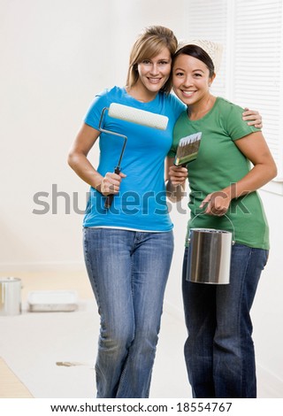 Self-sufficient friends painting with paint roller and paint brush and paint can and renovating home