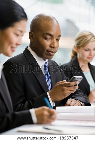 Serious businessman text messaging on cell phone in conference room