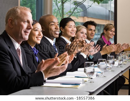 Multi-ethnic co-workers sitting in a row, applauding at conference table