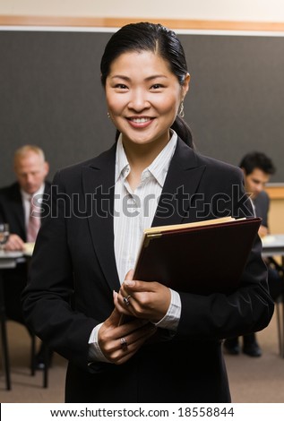 Confident Asian businessman holding files in front of co-workers in conference room