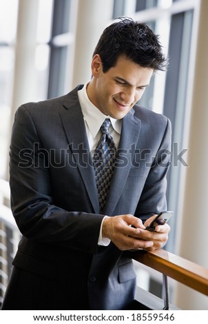 Businessman text messaging on cell phone in office lobby