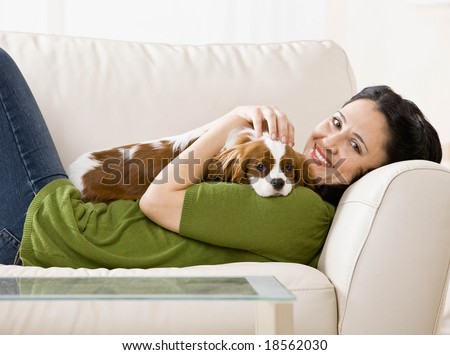 Relaxed woman laying on sofa holding and petting pet dog