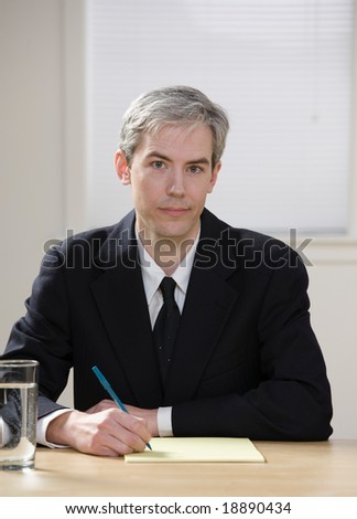 Serious businessman writing on legal pad taking notes