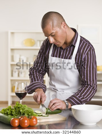 Attractive male cutting salad on the kitchen counter while drinking a glass of wine. vertical.