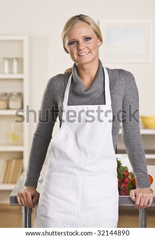 Young attractive blond with apron in the kitchen, leaning on the counter.