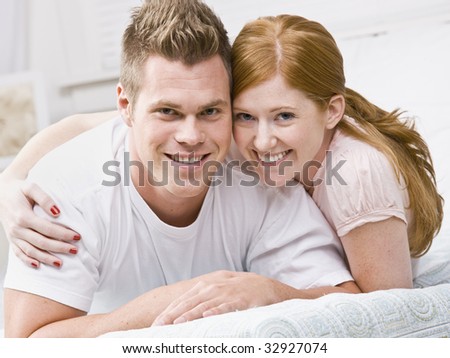 Smiling couple snuggling on bed. Square framed.