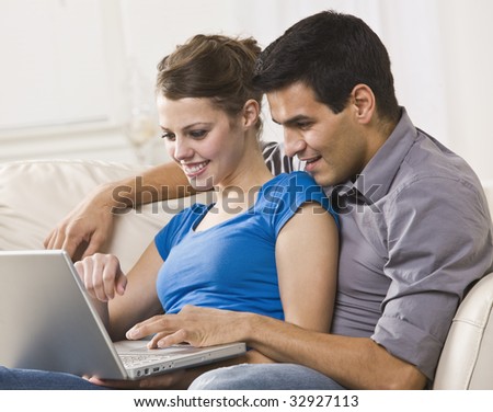 Attractive couple sitting together on a sofa and working on a laptop together. Horizontally framed photo.