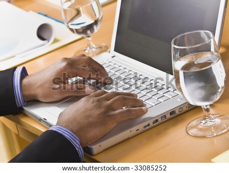 African American male hands typing on laptop keyboard. Glass of water on desk. Horizontal