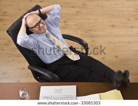 Attractive senior business man relaxing with feet on desk, reclining in chair, smiling at camera. Horizontal