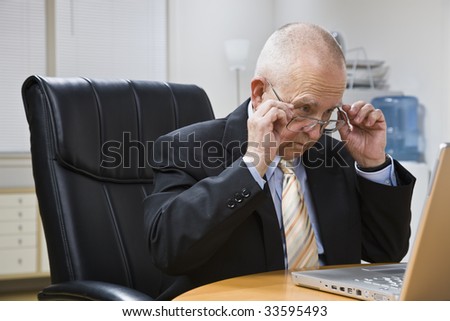 An elderly man is working on a laptop in an office.  Horizontally framed shot.