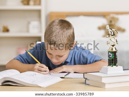 A young boy is working on his homework at the table.  He is looking away from the camera.  Horizontally framed shot.