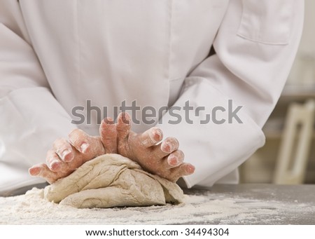 Chef standing over counter and kneading dough. Horizontal.