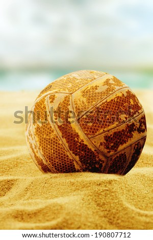 Old volleyball sits on top of the sand.