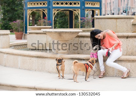 A young woman walking three dogs of pug breed.