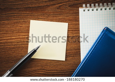 Blank notepad, notebook, sticker and pen showing on something on sticker on the office wooden table