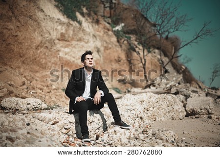 Fashion photo of a man on a seaside sitting on the stone