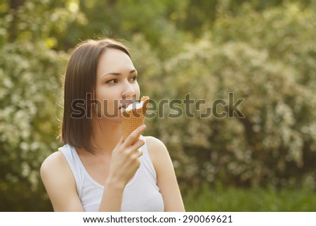 Photo of girl, eating ice-cream in white t-shirt on green blured background