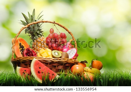Basket of tropical fruits on green grass.