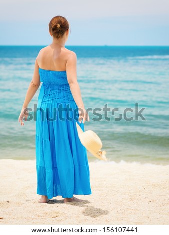 Woman in blue dress throws hat on the beach.