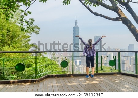 Young female tourist with raised arms to the sky enjoying awesome view of Taipei from top of mountain. Taipei skyline, Taiwan. Wonderful cityscape. Skyscrapers and other modern buildings of downtown. 商業照片 © 