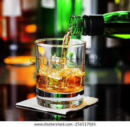 Whiskey pouring from a bottle into a glass in a bar. Scotch and Irish Single Malt or Blended Whiskey.