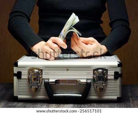 Storage and protection of cash and valuable items. Banking concept. Aluminum briefcase and a stack of hundred-dollar bills. Woman counting money. Money and documents in safe hands of bank employee.
