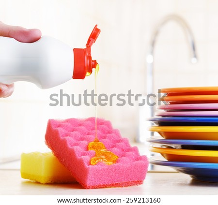 Several colorful plates, a kitchen sponges and a plastic bottle with natural dishwashing liquid soap in use for hand dishwashing. Eco-friendly, toxin-free, green cleaning product. Dishwashing concept.