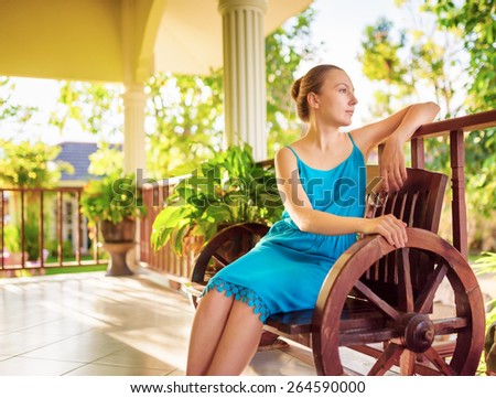Young woman in blue dress relaxing in house terrace. Outdoor portrait.