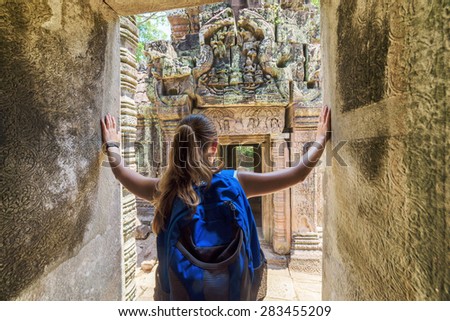 Young female tourist with blue backpack coming to ancient Preah Khan temple in Angkor and looking at the bas-reliefs on the walls and on mysterious ruins. Siem Reap, Cambodia.