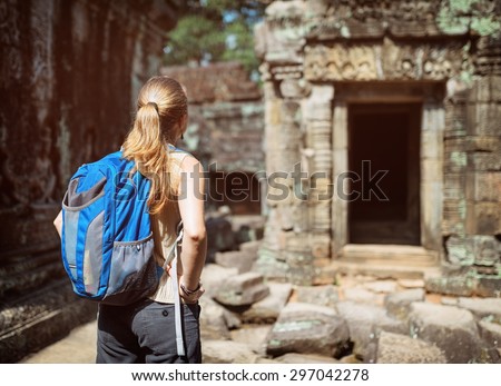 Young female tourist with blue backpack exploring mysterious ruins of ancient Preah Khan temple in Angkor. Siem Reap, Cambodia.