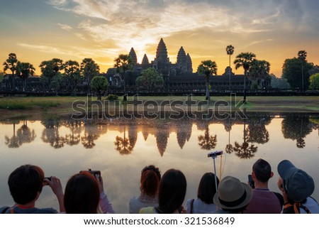 Many Asian tourists taking picture of ancient temple Angkor Wat at sunrise. Siem Reap, Cambodia. Towers of Angkor Wat reflected in lake at dawn. Angkor Wat is a popular tourist attraction.