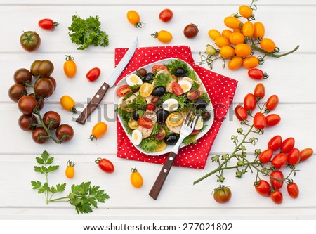 Salad with chicken, tomatoes, olives, lettuce, quail eggs and olive oil on a white wooden table with variety of tomatoes, top view
